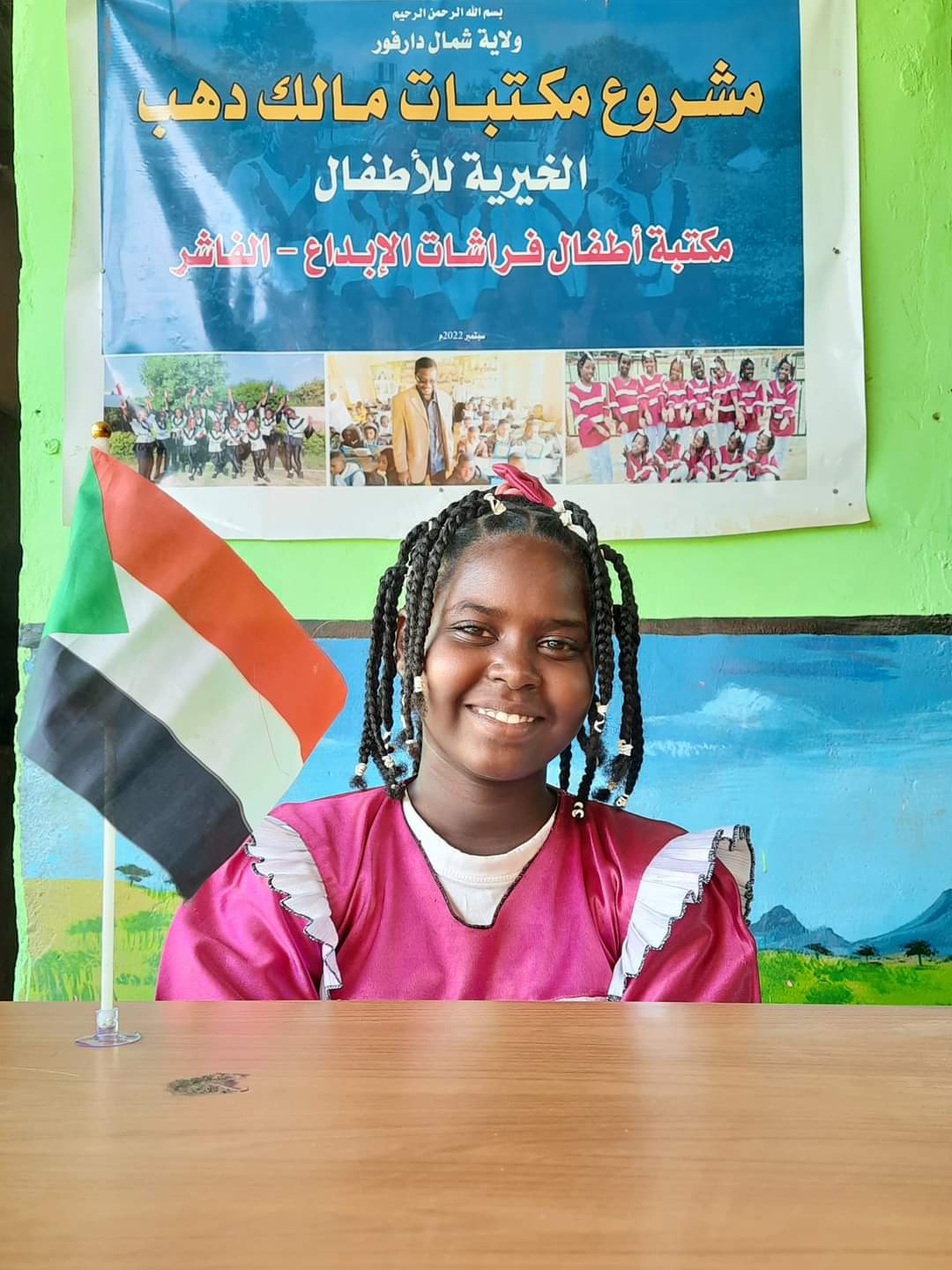 طفلة وعلم السودان ولافتة مكتبة الأستاذ دهب