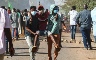شابان يحملان متظاهرًا في أحد المواكب الرافضة للحكم العسكري بالخرطوم