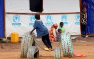 أطفال لاجئون سودانيون وأمهم أمام خيمة بها شعار UNHCR